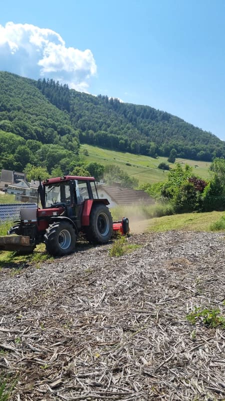 Traktor mit Heckmulcher über einem Eifeldorf