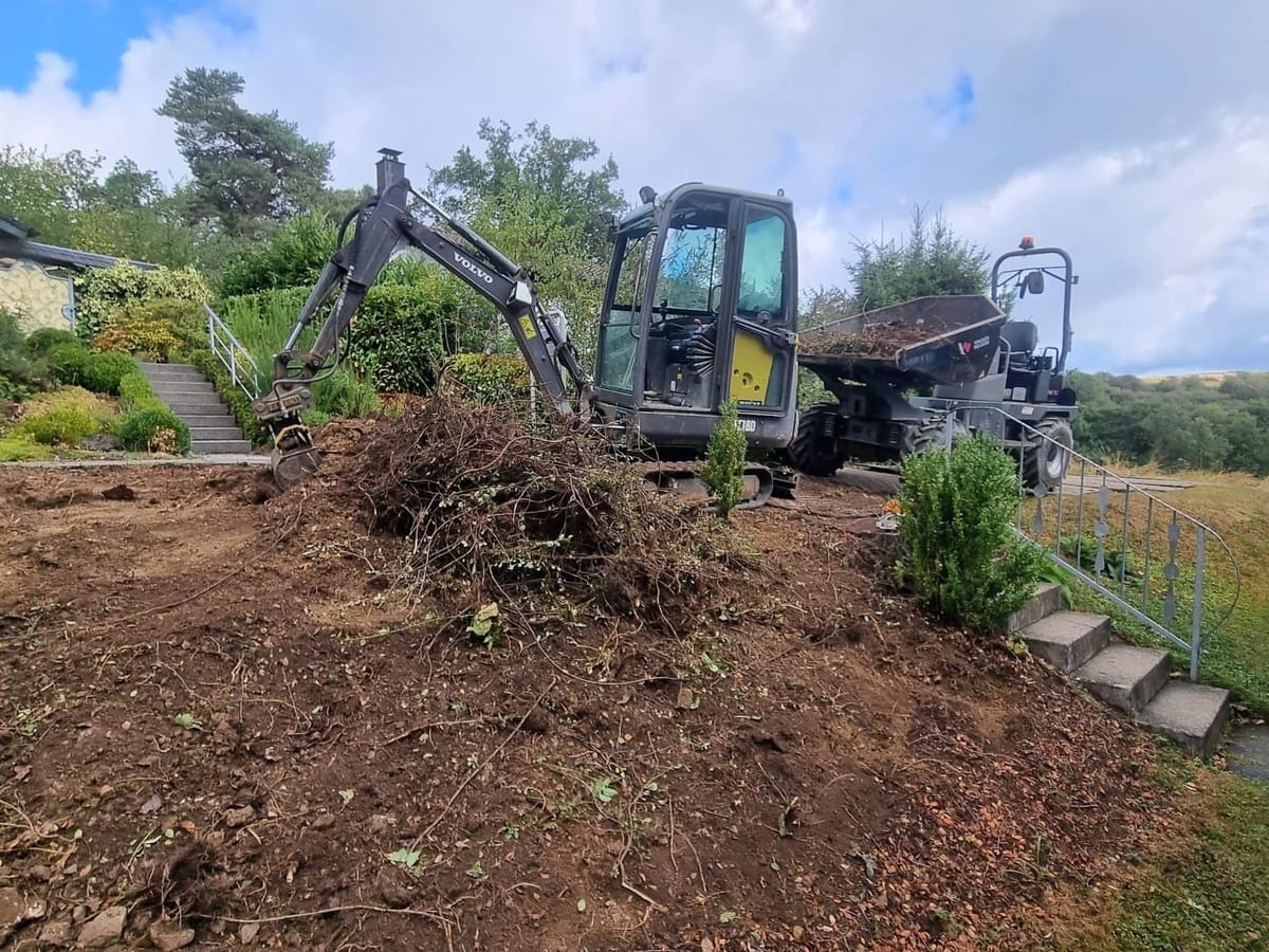 Minibagger rodet Sträucher an einem Gartenhang